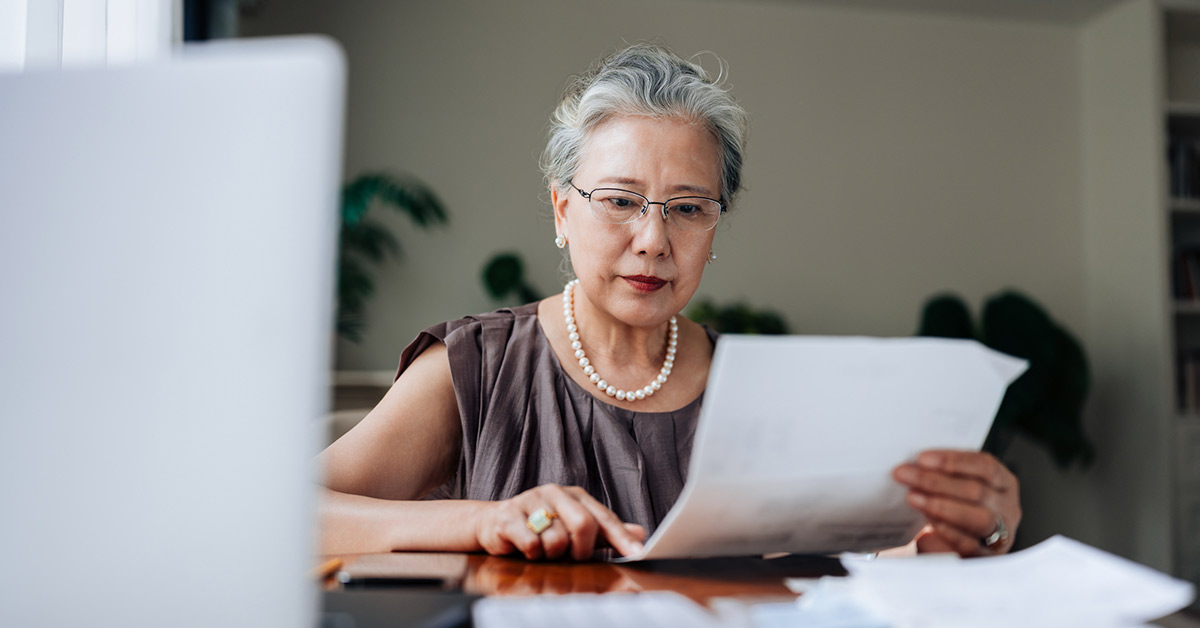 Older woman wearing glasses and nice jewelry examining a document.
